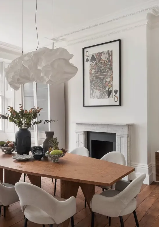 Dining room with a timber table, white chairs, a sculptural pendant and a marble fireplace