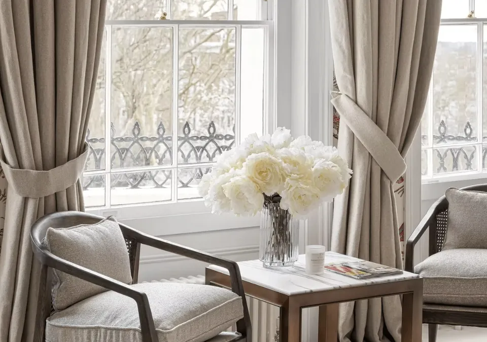 Two armchairs and a side table with flowers by a window with heavy curtains