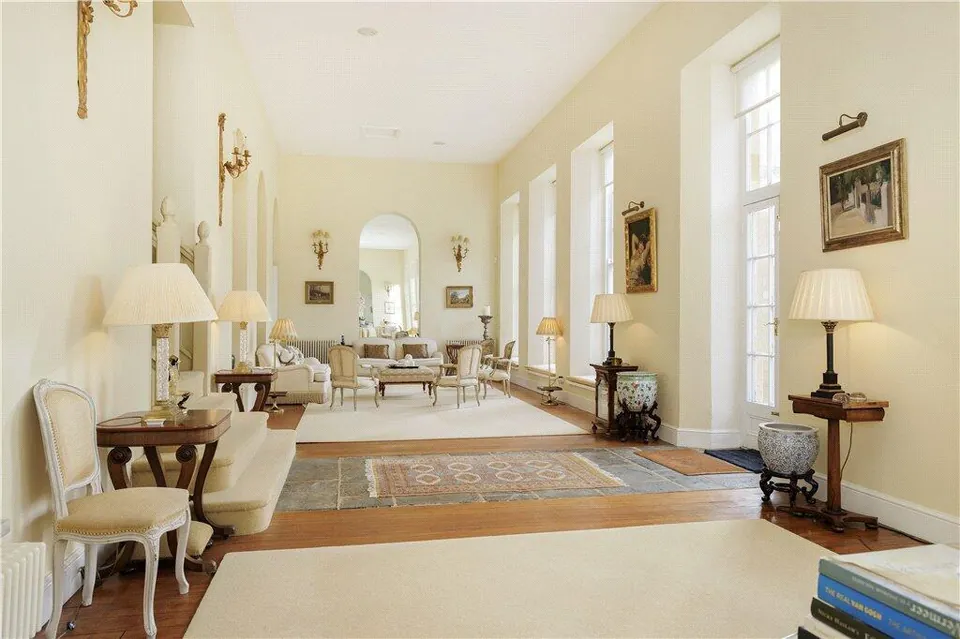 Long period drawing room with tall windows, lamps and a rug