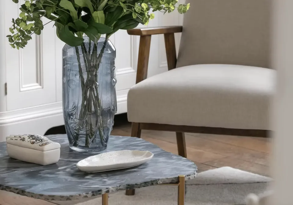Marble side table with a glass vase beside an upholstered armchair
