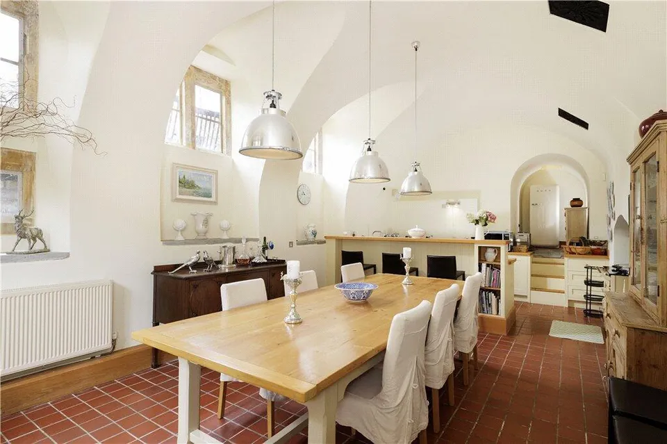 Kitchen with a long timber dining table, pendant lights and a terracotta tiled floor