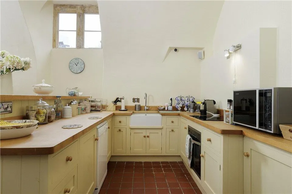Cream fitted kitchen with timber worktops and a terracotta tiled floor