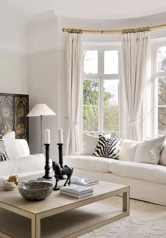 Bright living room with white sofas and tall curtained windows